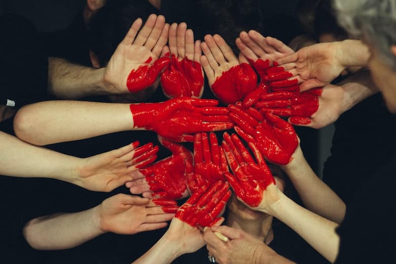 A volunteer of many hands put together in a circle formation. there is red paint on each hand which makes a heart when put together.