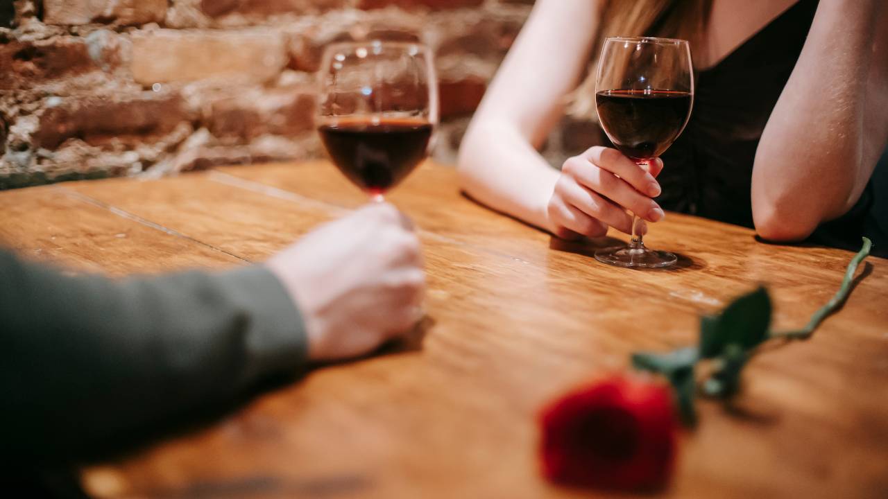 man and woman resting arms on table with a rose and two glasses of wine