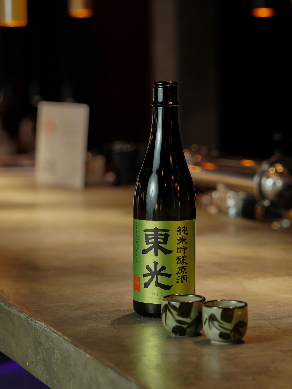 A bottle of sake with two sake cups at a bar.