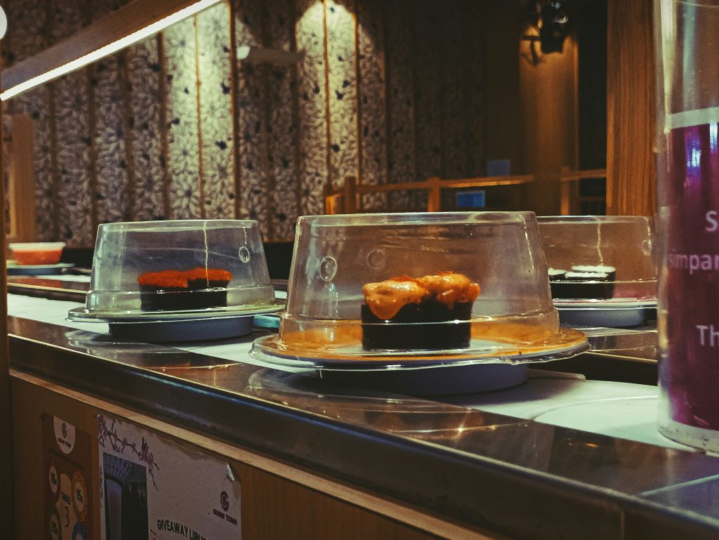 A couple of sushi plates, each with sushi arranged on them, on a conveyor belt in a best sushi restaurants in Tokyo as traditional sushi train .