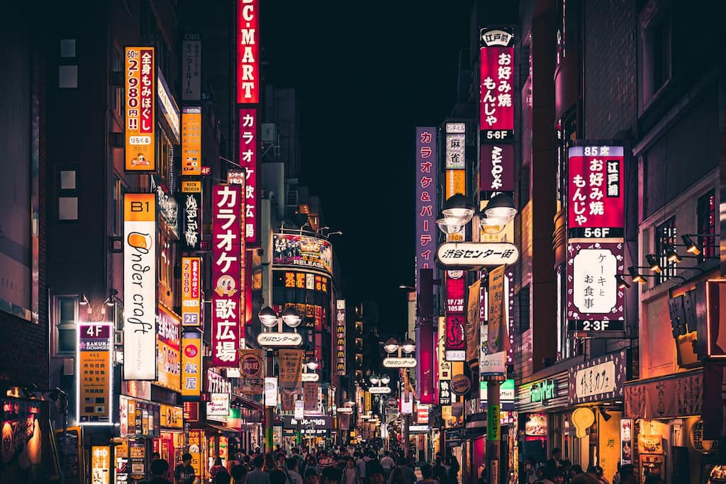 Image of a vibrant street in Shibuya often visited by foreigners living in Tokyo at night. There are different night life eateries and entertainment in the image.