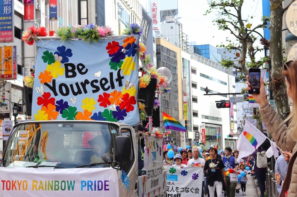 Image showing the Tokyo Pride walk that is popular with LGBTQ+ members and supporters living in tokyo. They are carrying rainbow pride flags and other signs to give support to LGBTQ+ causes.