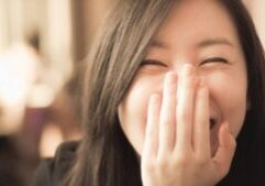 Asian woman smiling with hand in front of face